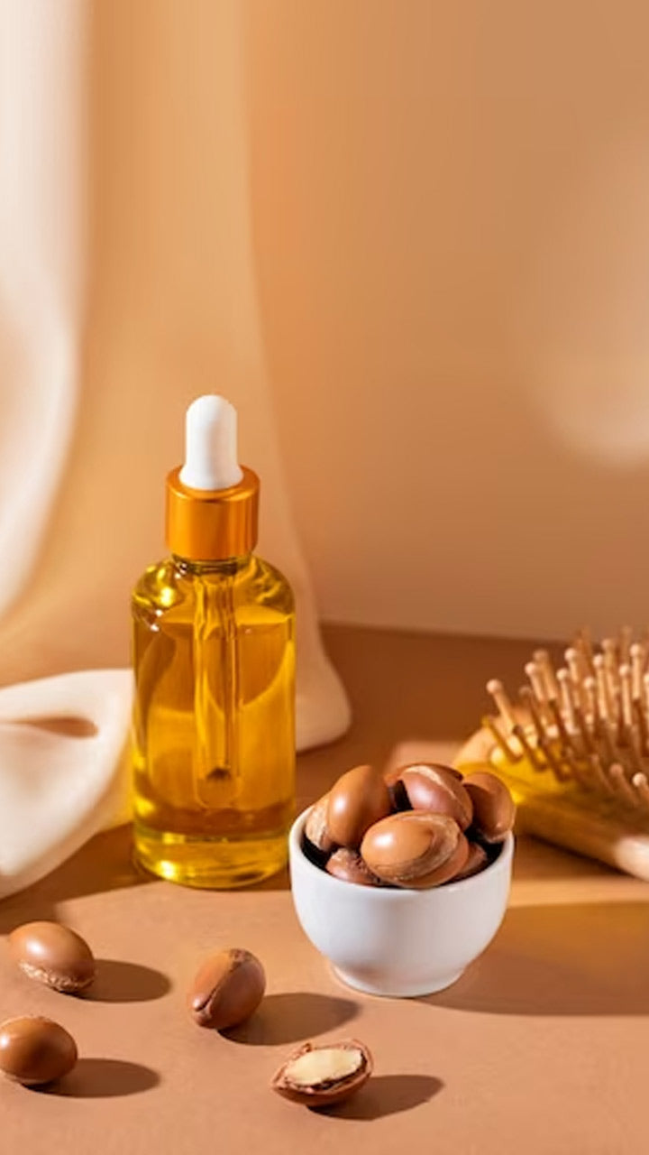 Lottiee Duty Pure Argan Oil in a clear glass bottle with a white dropper and gold cap, displayed alongside argan nuts in a small white bowl, set against a warm beige background.