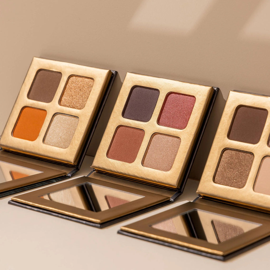 Three eye shadow palettes by Lottiee Duty feature a variety of shades, including warm browns, oranges, and shimmering golds. Each palette has four colors and a reflective mirror in the base.