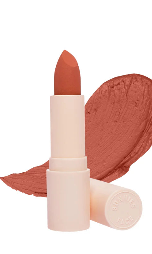 Lottiee Duty Organic Waterproof Matte Lipstick in a warm peachy hue, showcased with a creamy texture. The lipstick case is sleek with a matte finish, complementing the product's natural look, against a background of painted swatch.