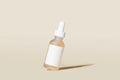 Lottiee Duty Hydrate & Luminate Elixir Serum in a clear glass dropper bottle with a white lid. The serum inside appears orange and the bottle features a blank white label.