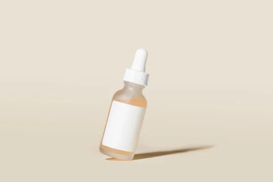 Lottiee Duty Hydrate & Luminate Elixir Serum in a clear glass dropper bottle with a white lid. The serum inside appears orange and the bottle features a blank white label.